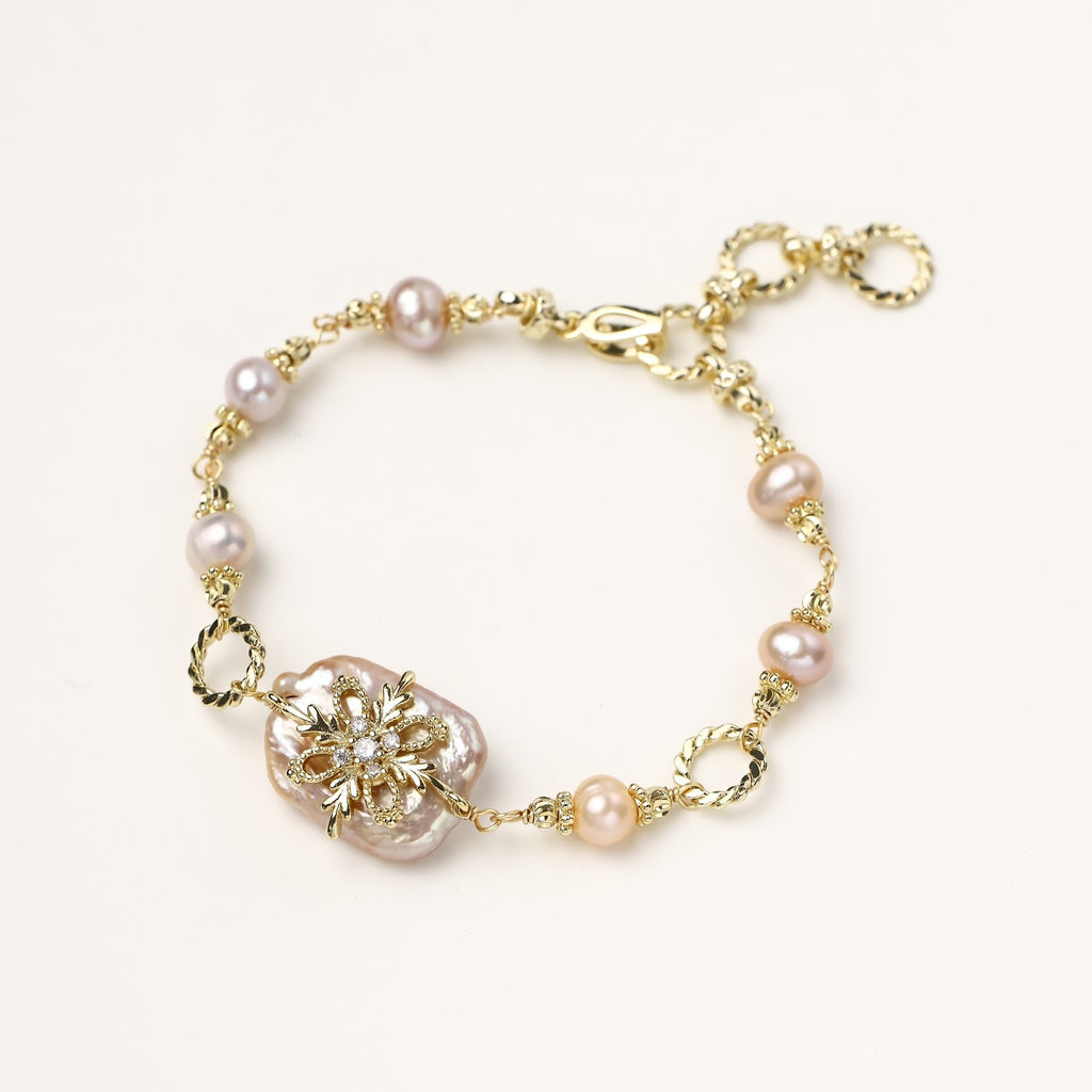Gold-plated chain bracelet with baroque pearl centerpiece and floral charm, featuring mixed freshwater pearls.