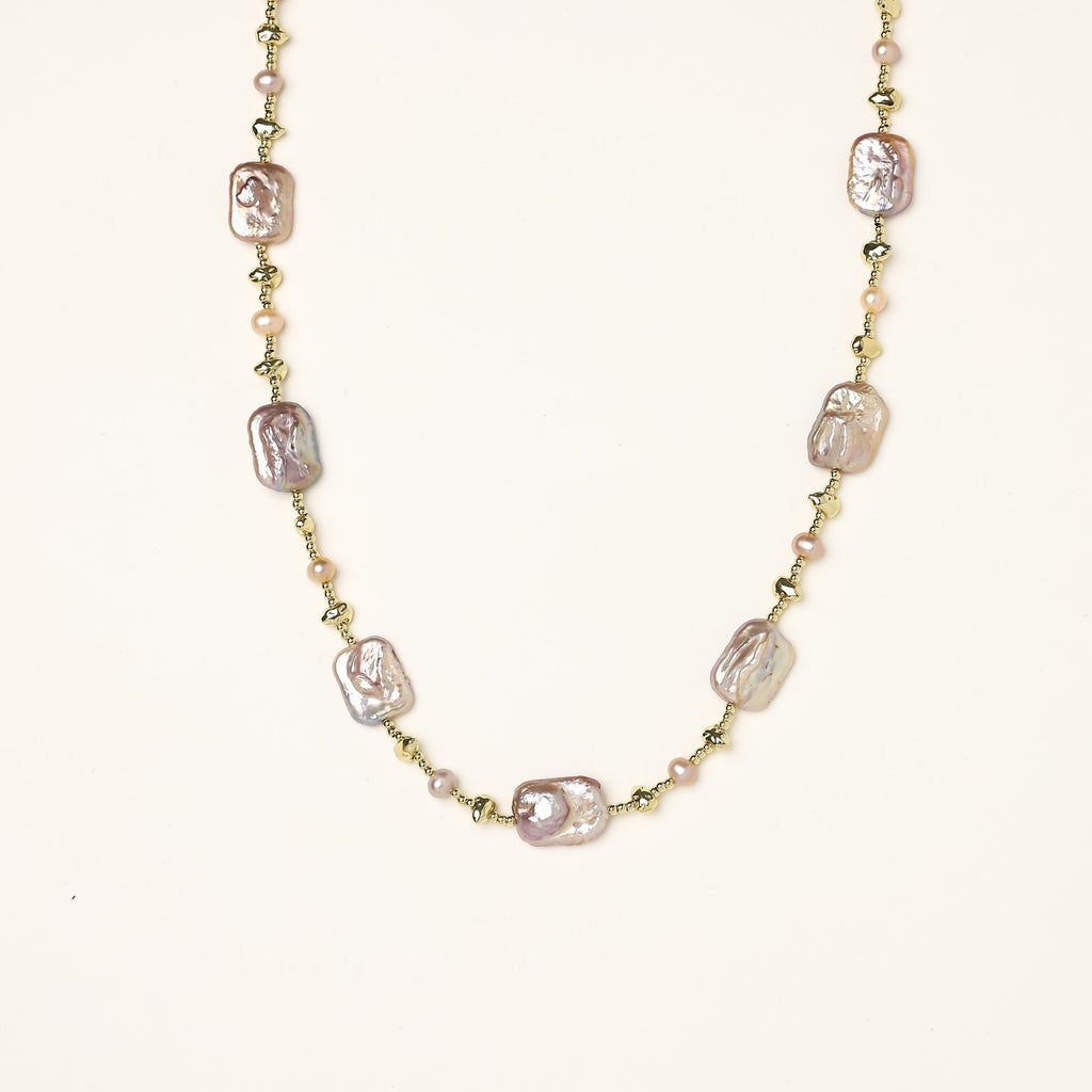 Long gold-plated necklace with iridescent baroque pearls and round freshwater pearls on cream background