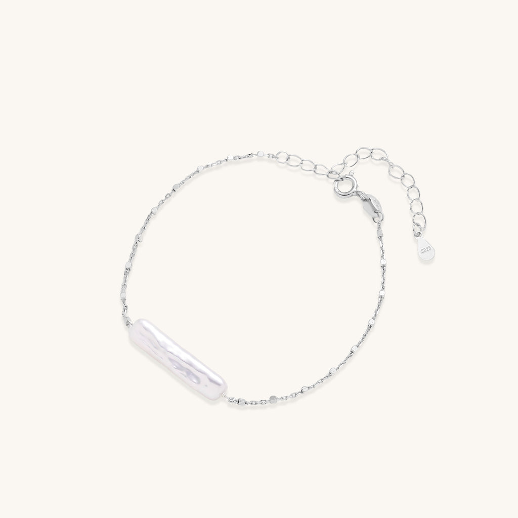 Delicate sterling silver chain bracelet with an organic white baroque pearl centerpiece on neutral background