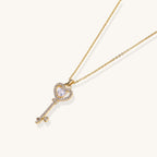 Gold-plated key pendant necklace with heart top and crystal embellishments on adjustable chain against cream background