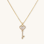 Gold-plated key pendant necklace with heart top and crystal embellishments on adjustable chain against cream background