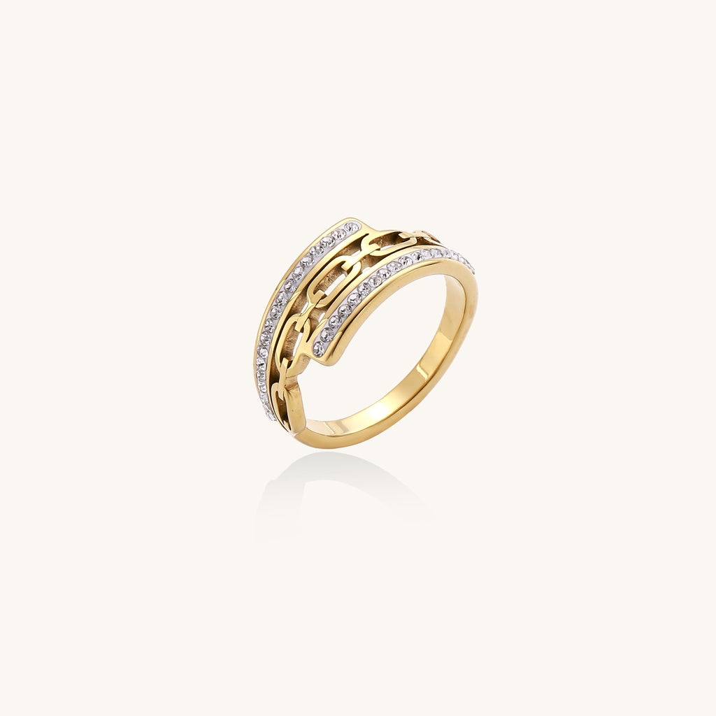 Gold-plated chain-link ring with rhinestone rows on cream background, showing bold geometric design and sparkling details.