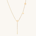 Gold-plated lariat necklace spelling LOVE with letter charms and vertical bar pendant on white background.