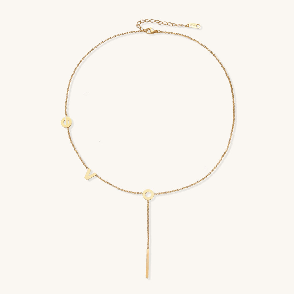 Gold-plated lariat necklace spelling LOVE with letter charms and vertical bar pendant on white background.